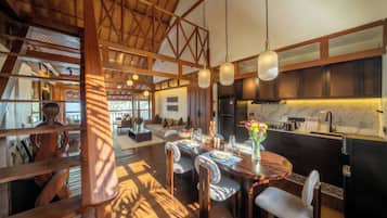 A spacious dining area with a wooden table set for a meal, a kitchen with modern appliances, and a view of the outdoors through large windows.
