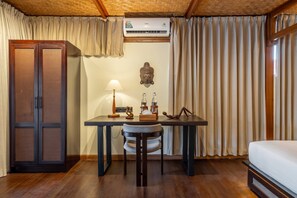 Een kamer met een houten plafond, een bed, een bureau met een lamp, een Boeddhabeeld en een kledingkast.
