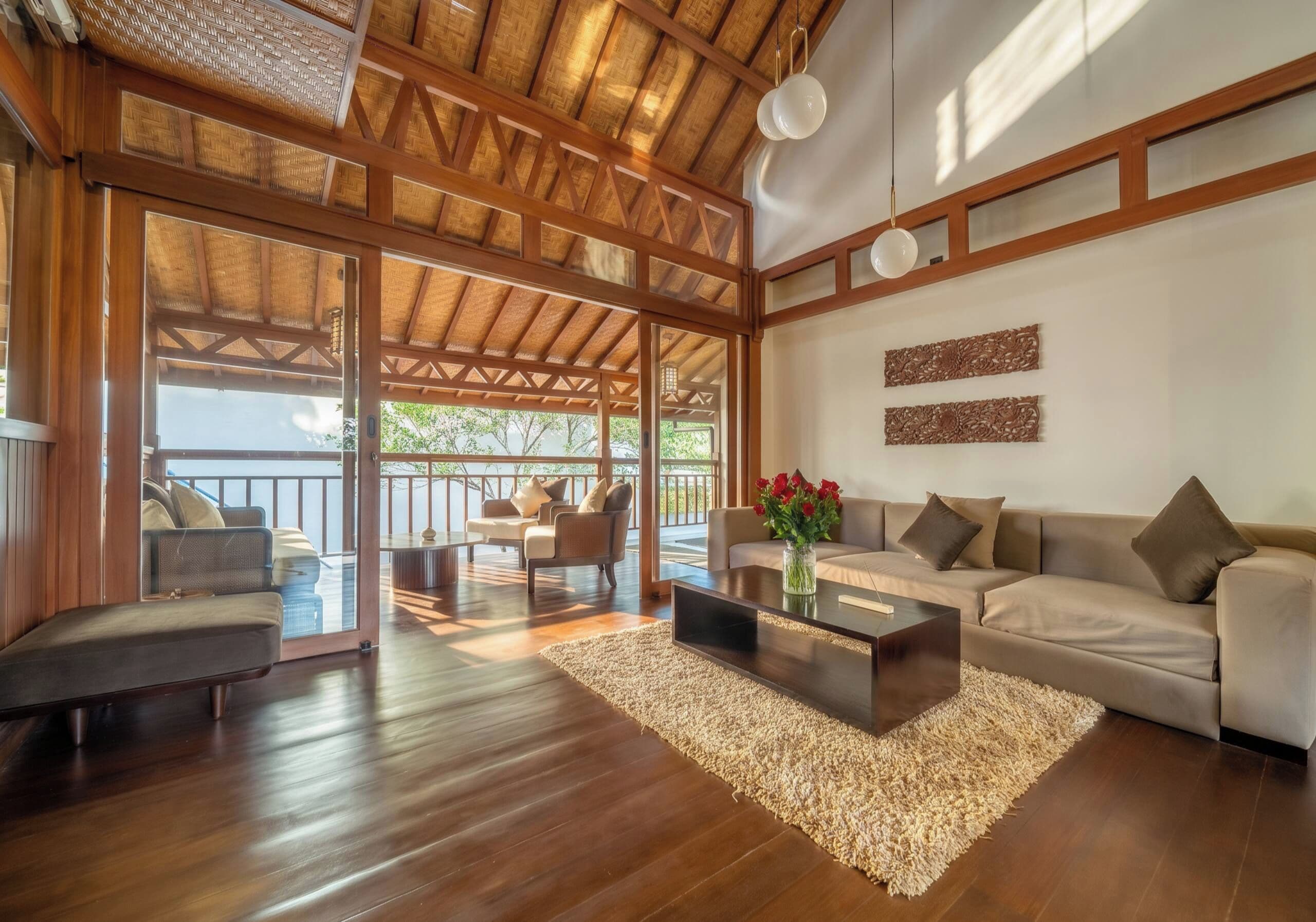 A spacious living area with a wooden ceiling, a sofa set, a coffee table, and a view through glass doors to an outdoor deck.