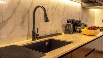 Una cocina con un lavabo negro, una cafetera y un frutero en la encimera.