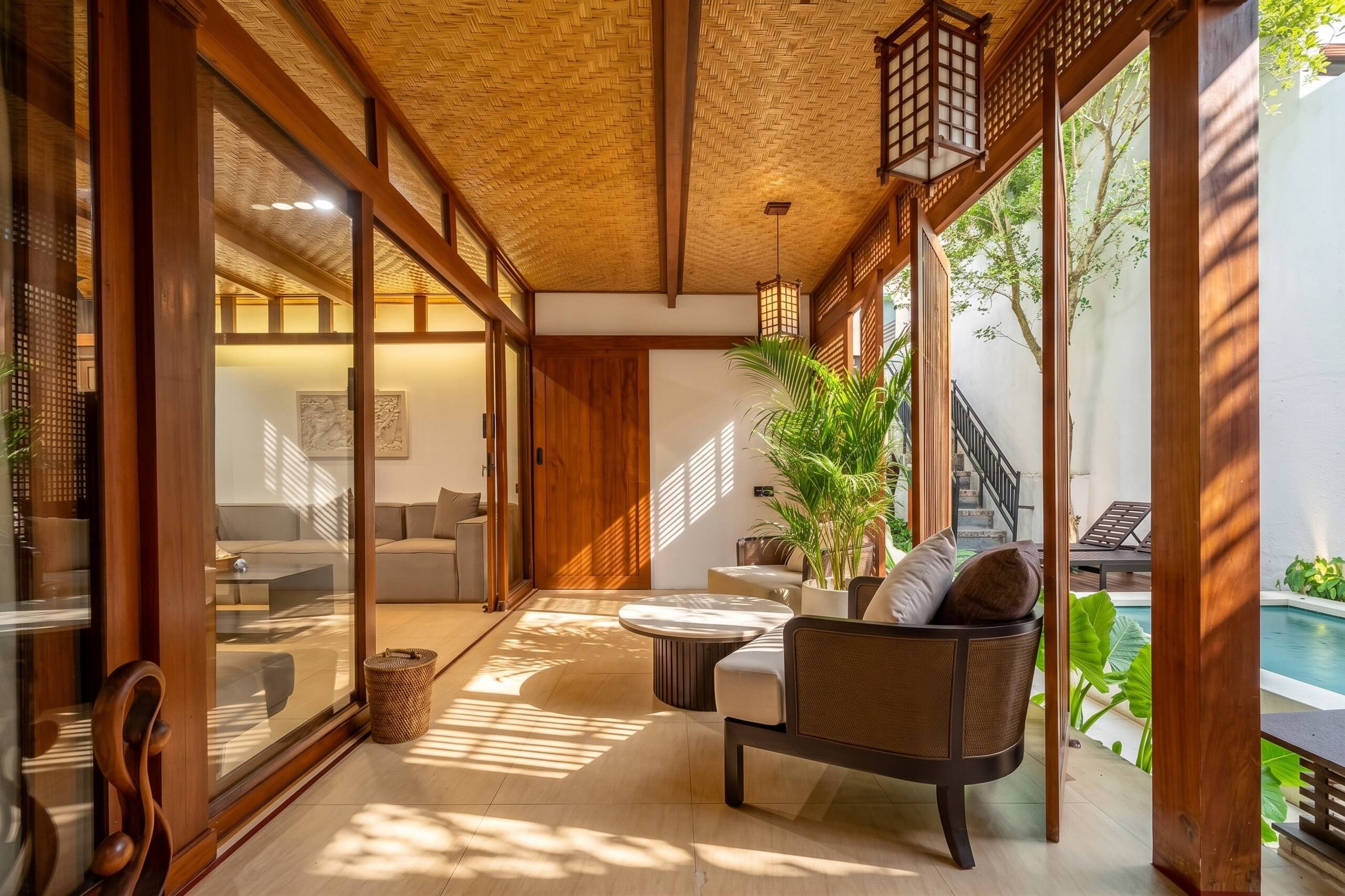 Un interior moderno con techo de madera, puertas de cristal correderas, una zona de estar con mesa redonda y vistas a una piscina.