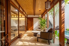 Un interior moderno con techo de madera, puertas de cristal correderas, una zona de estar con mesa redonda y vistas a una piscina.