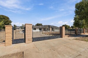 A gated entrance with a paved driveway leading to a building with a brick facade. - Welcome to your private retreat situated on over an acre lot with pool/spa (Visalia)