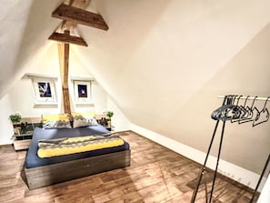 A bedroom with a bed, a wooden beam ceiling, a window, and a clothes drying rack. - Villa Klarka by Interhome (Rokytnice nad Jizerou)