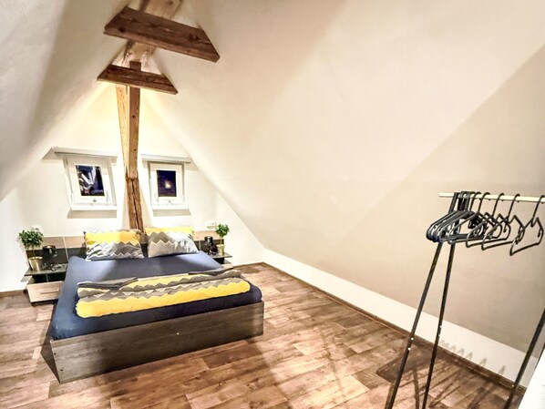 Een slaapkamer met een bed, een plafond met houten balken, een raam en een droogrek.