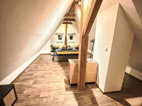 Et soveværelse med skråvæg, trægulv, seng med puder, et natbord og et vindue.