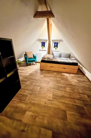Slaapkamer in loftstijl met schuine wanden, een houten bed, een stoel en twee ramen met planten.