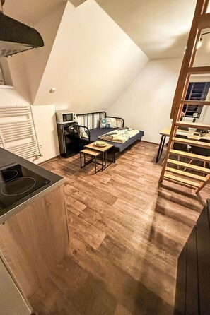 Een ruimtelijke leefruimte met een kitchenette, een bank, een eettafel en een houten trap.
