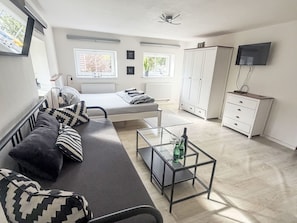 A modern living room with a sofa, a glass coffee table, a bed, a wardrobe, and a TV. - Villa Klarka by Interhome (Rokytnice nad Jizerou)