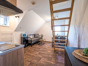 Ein Loft-Zimmer mit schrägem Dach, einer Küchenzeile, einem Sofa, einer Leitern und einem Essbereich.