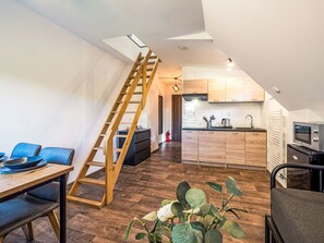 A modern kitchen with wooden cabinets, a built-in oven, and a dining area with a wooden table and blue chairs. - Klarka 4 by Interhome (Rokytnice nad Jizerou)