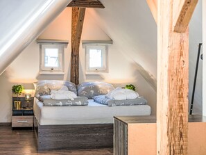 A bedroom with a sloped ceiling, a bed with multiple pillows, a nightstand with a lamp, and two windows. - Klarka 4 by Interhome (Rokytnice nad Jizerou)