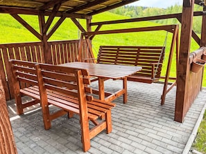 Ein hölzerner Außenbereich mit Bänken und einem Tisch, umgeben von einer Holzpergola und Backsteinböden.