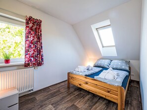 A bedroom with a sloped ceiling, a skylight, a bed with towels, a radiator, and a window with curtains. - Klarka 3 by Interhome (Rokytnice nad Jizerou)
