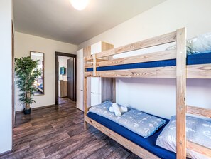 Een slaapkamer met stapelbed, houten vloer, een potplant en een spiegel.