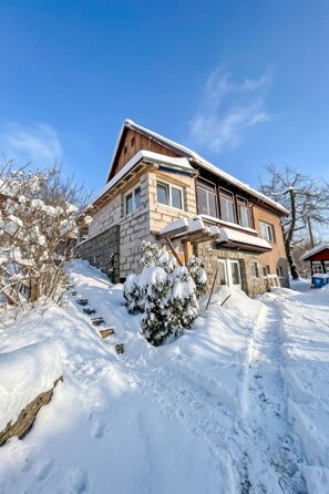 A two-story house with a stone facade and a wooden roof, surrounded by snow-covered ground and trees. - Klarka 1 by Interhome (Rokytnice nad Jizerou)