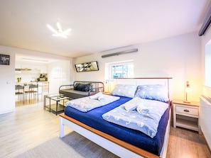 Een moderne slaapkamer met een groot bed, nachtkastjes, een bureau en uitzicht op de keuken.