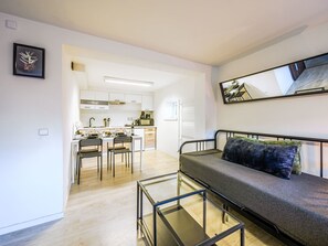 Een ruimtelijk ingerichte leefruimte met een kitchenette, een eethoek en een bank met een glazen bijzettafeltje.