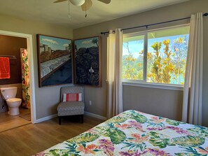 Quarto com cama, janela com cortinas, uma cadeira e obras de arte na parede.