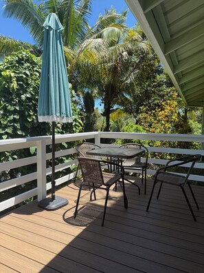 Um deck de madeira com guarda-corrimão branco, uma mesa com cadeiras e um guarda-sol verde.