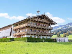 Un edificio de madera de varios pisos con balcones, rodeado de un césped cuidado y con montañas al fondo.