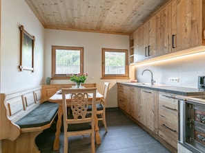 A kitchen with wooden cabinets, a dining table with chairs, a bench, and a window with a view of trees. - Tyrolean farmhouse apartment with terrace (Kirchberg in Tirol)