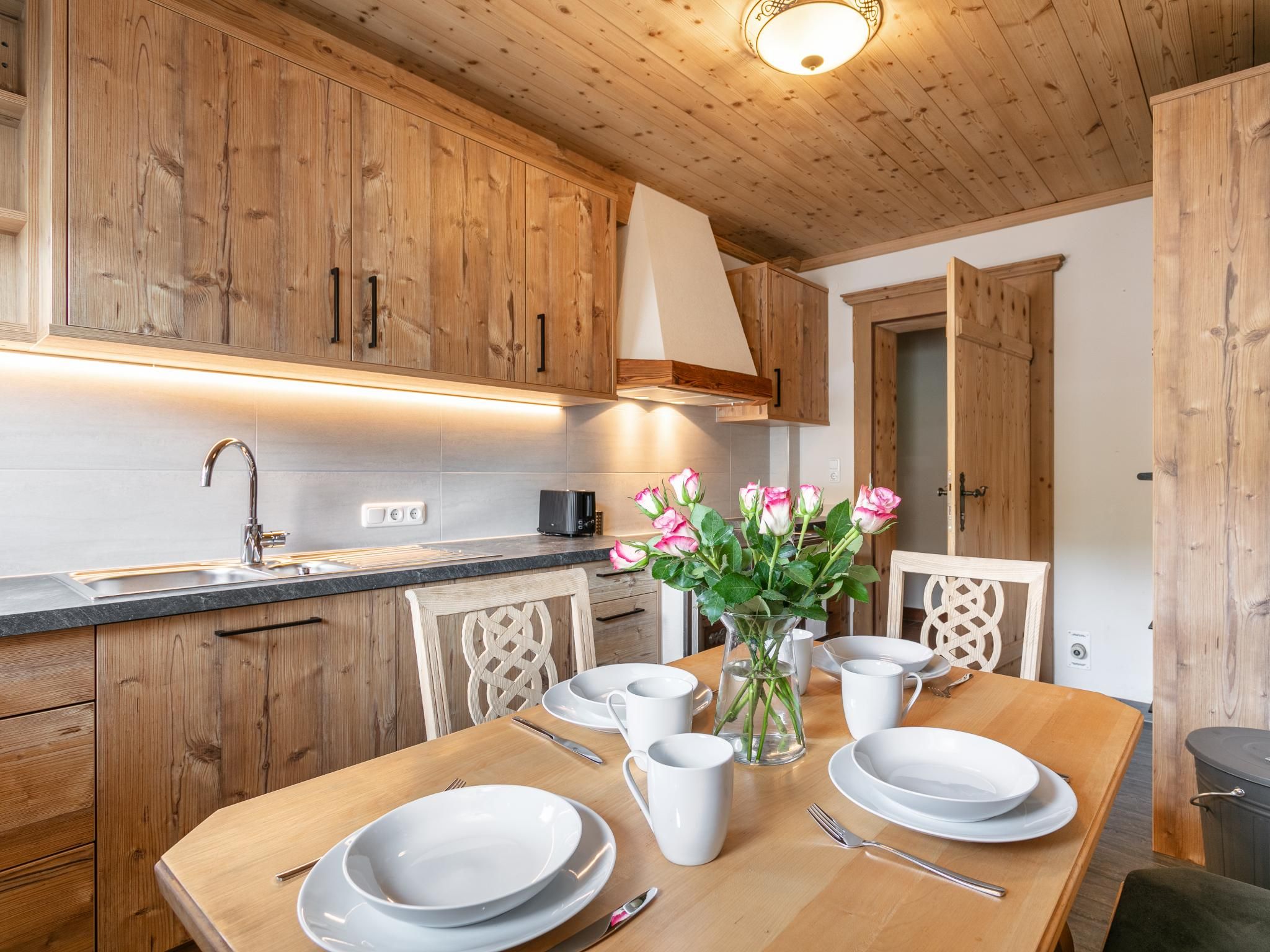 Una cucina in legno con un tavolo da pranzo apparecchiato per due persone, una macchina del caffè e un vaso con fiori.
