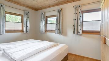 A room with a bed, wooden ceiling, windows with curtains, and a wooden floor.