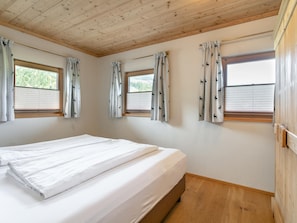 Una habitación con cama, techo de madera, ventanas con cortinas y piso de madera.