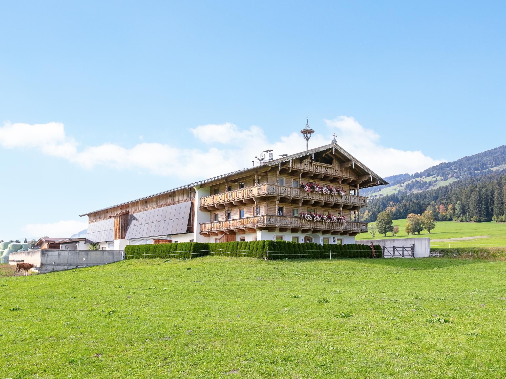 Un edificio de madera de varios pisos con balcones, rodeado por un campo verde y montañas al fondo.