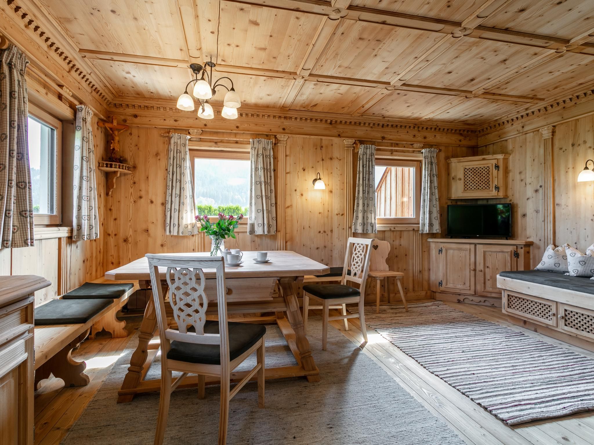 A wooden cabin interior with a dining table, chairs, a sofa, a television, and a fireplace.
