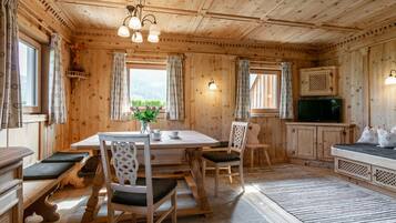 A wooden cabin interior with a dining table, chairs, a sofa, a television, and a fireplace.