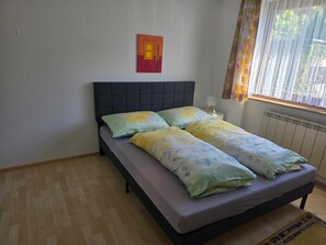 Quarto com cama, janela com cortinas, radiador e uma obra de arte na parede.