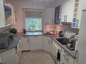 A compact kitchen with white cabinets, a microwave, a coffee maker, and a window with a view of greenery. - Cozy apartment with a view of Lake Constance (Hörbranz)