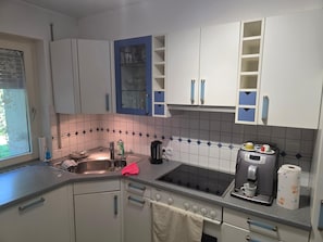 Cozinha com armários brancos, pia, fogão e cafeteira.