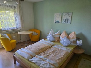 A bedroom with a bed, two yellow chairs, a small round table, and two wall-mounted artworks. - Cozy apartment with a view of Lake Constance (Hörbranz)