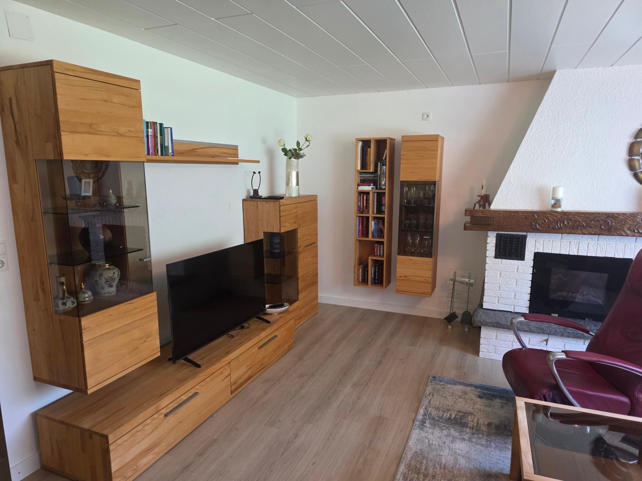 A modern living room with a flat-screen TV, wooden furniture, a fireplace, and a red chair.