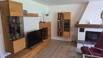 A modern living room with a flat-screen TV, wooden furniture, a fireplace, and a red chair.