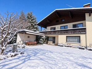 A two-story building with a balcony, a covered outdoor seating area, and snow-covered surroundings. - Cozy apartment with a view of Lake Constance (Hörbranz)