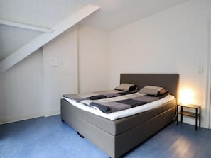 Ein Schlafzimmer mit einem Bett, einem Nachttisch und einer schrägen Decke.