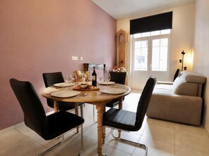 A dining area with a round table set for four, surrounded by black chairs. A wooden cabinet with a clock is visible in the background. - Nice little cottage in the heart of Dinant! (Dinant)