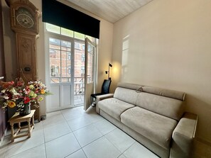 A living room with a beige sofa, a wooden clock, and a vase of flowers. - Nice little cottage in the heart of Dinant! (Dinant)