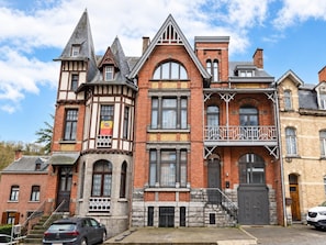 A historic building with multiple architectural styles, including a tower, a balcony, and a staircase leading to the entrance. - Group house in a typical style in Dinant (Dinant)