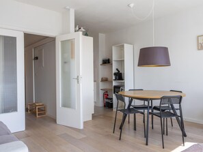 A modern living space with a dining area featuring a round wooden table and black chairs, a white cabinet with a glass door, and a hanging pendant light. - Bright studio on the 7th floor (Middelkerke)