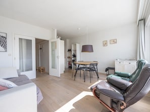 A modern living room with a sofa, a dining table with chairs, a lamp, and a view of the kitchen. - Bright studio on the 7th floor (Middelkerke)
