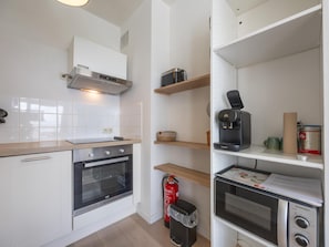 A modern kitchen with white cabinetry, a built-in oven, a coffee machine, and a fire extinguisher. - Bright studio on the 7th floor (Middelkerke)