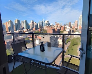 Varanda com mesa e cadeiras, vista para uma paisagem urbana com diversos edifícios.