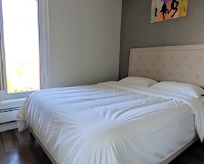 Ein Bett mit weißer Bettwäsche in einem Zimmer mit Fenster und Wandgemälde.