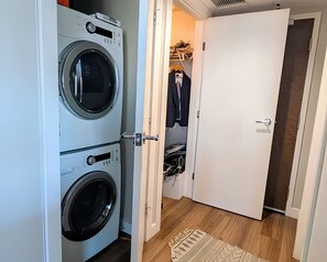 Ein Waschraum mit gestapelten Waschmaschinen und einer Tür zu einem Schrank mit aufgehängter Kleidung.