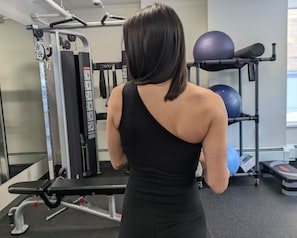 Ein Fitnessraum mit Trainingsgeräten, einer Bank und einem an der Wand befestigten Medizinballständer.